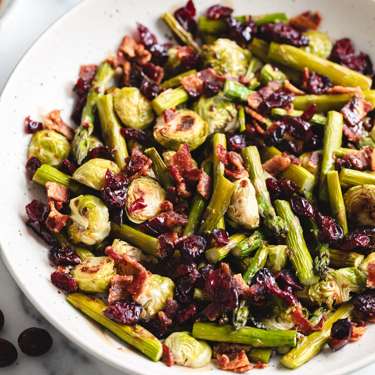 Close up view of asparagus, cranberries, bacon, and brussels sprouts.