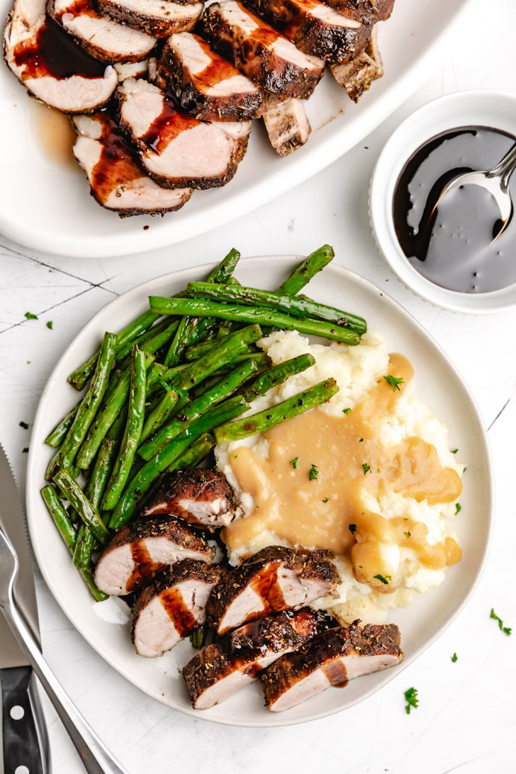 Top down view of pork tenderloin on a plate of mashed potatoes and green beans.