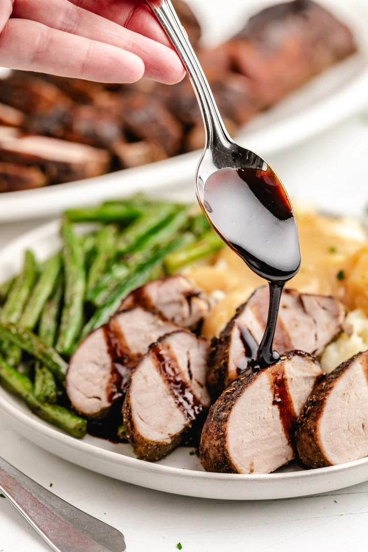 Spoon drizzling glaze over a balsamic pork tenderloin.