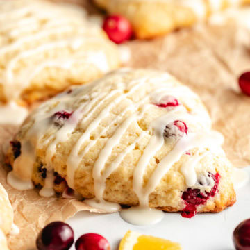 Close-up of a glazed cranberry orange scone with fresh cranberries and orange slices nearby.