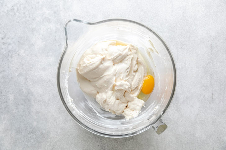 Egg added to a bowl of cream cheese and sugar.