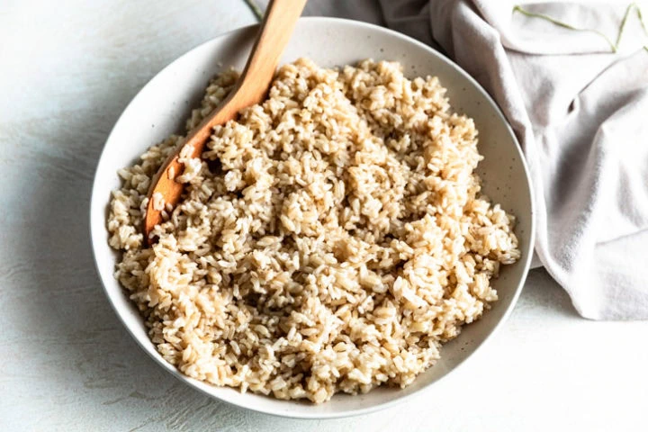 Brown spoon laid in a bowl of rice.