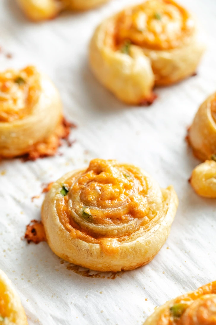 Flaky jalapeño popper pinwheels on a baking sheet.