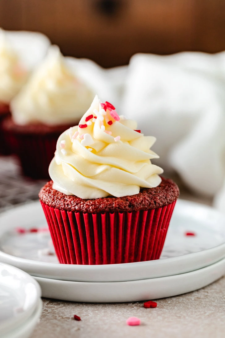 Sprinkles and frosting on top of a red velvet cupcake.