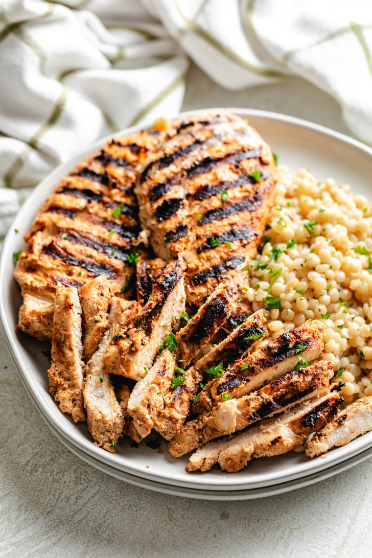 Sliced yogurt martinated chicken next to couscous.