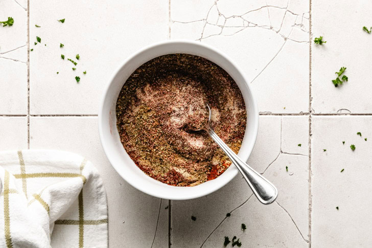 A spoon mixing a blend of spices in a white bowl.