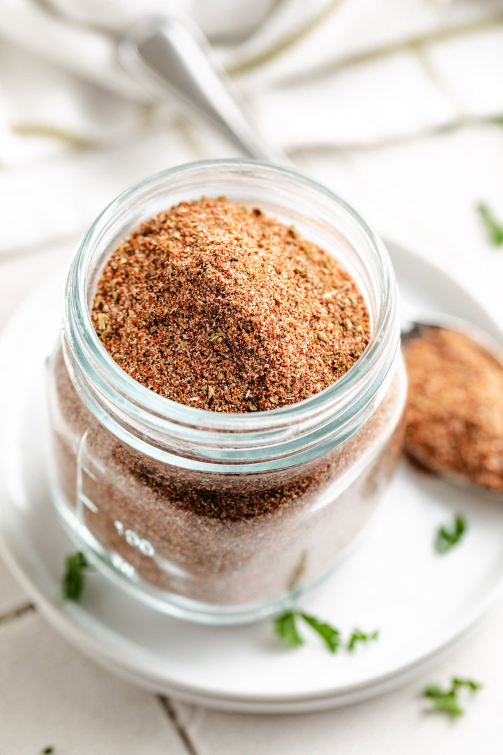 A spoonful of chili seasoning next to a glass jar.