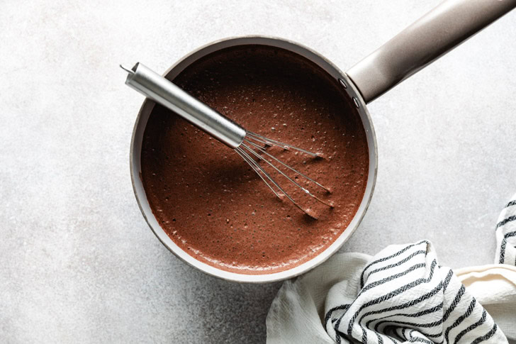 A saucepan with a whisk resting inside, filled with freshly made chocolate mixture.