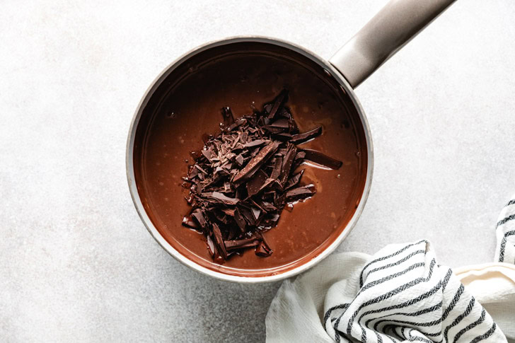 Finely chopped chocolate being added to a saucepan of warm pudding mixture.