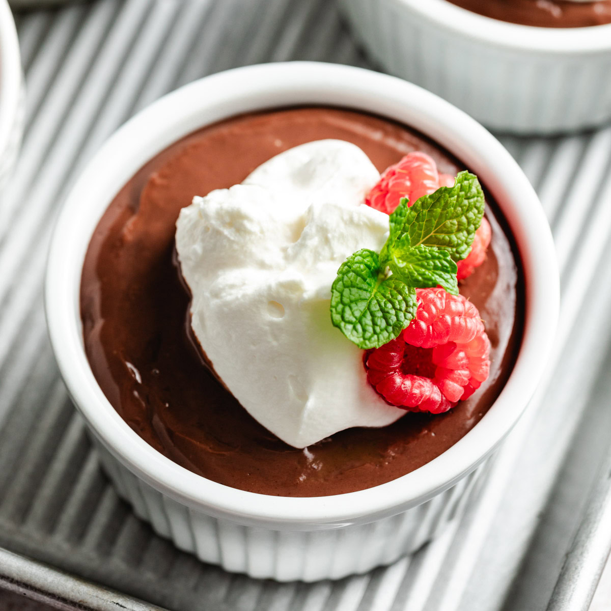 A close-up shot of chocolate pudding in a ramekin, topped with whipped cream and fresh berries.