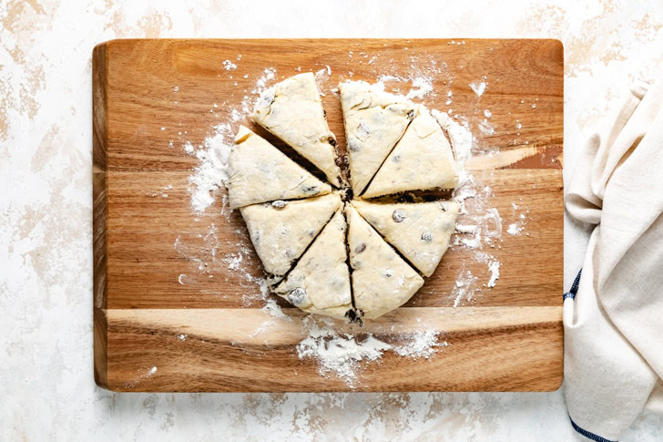 Scone dough cut into wedges on a floured wooden board.