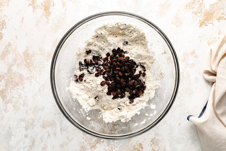 Mixing raisins into dry ingredients in a glass bowl.