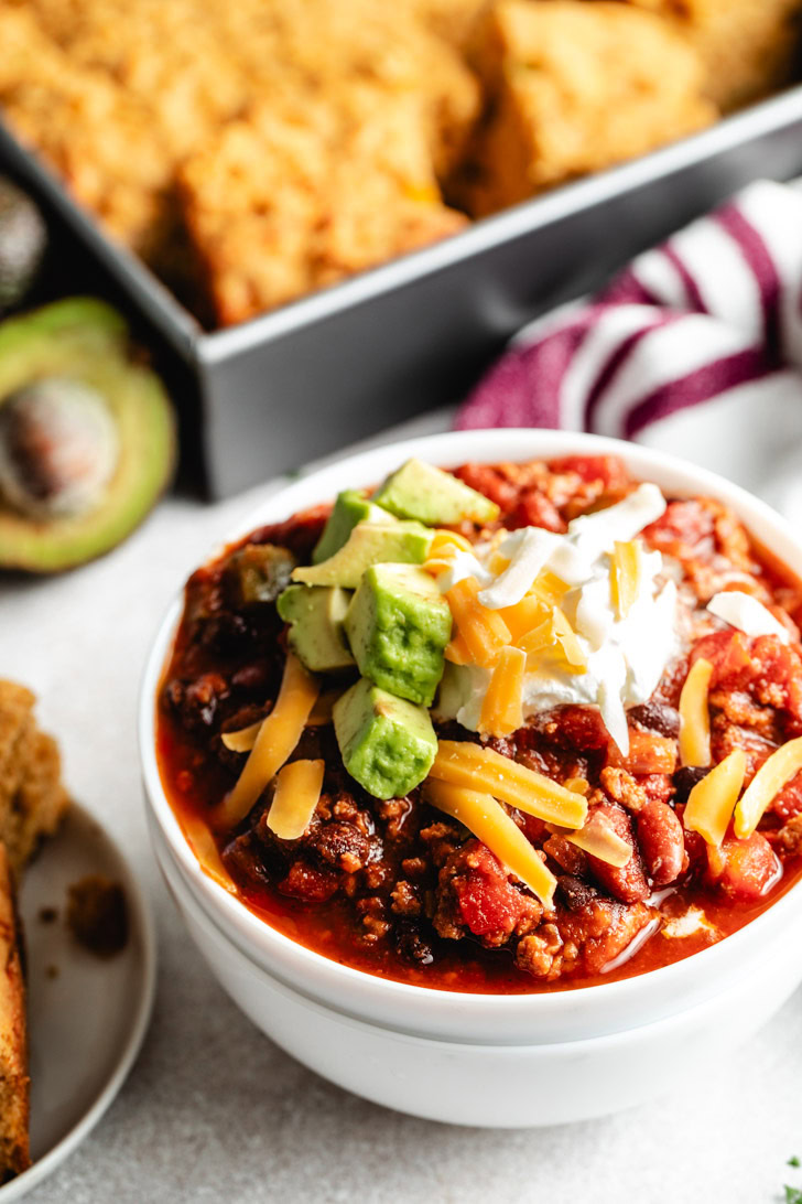 A top-down view of a turkey chili bowl with melted cheese and a side of cornbread.