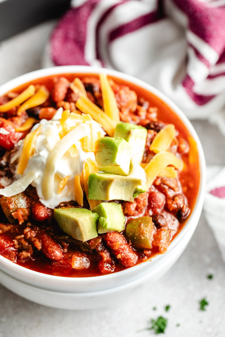 A white bowl of chili with toppings.