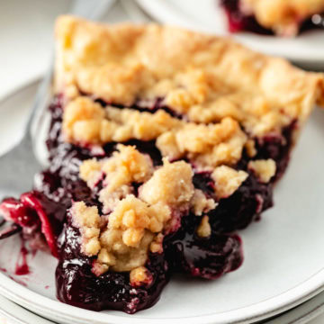 A slice of cherry pie with a golden brown crumb topping and thick cherry filling.