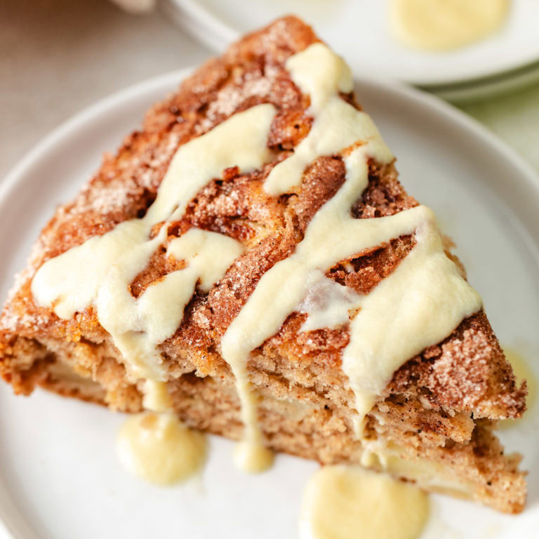 A slice of irish apple cake drizzled with warm custard sauce on a white plate.