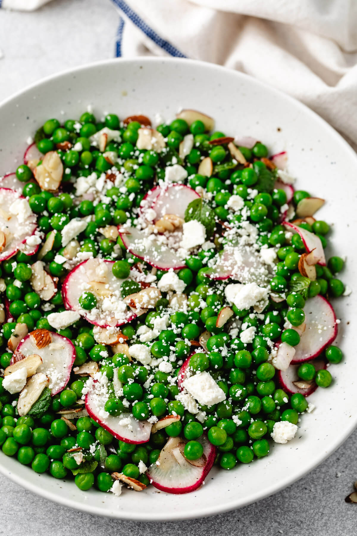 Close-up of a bowl of pea salad with feta, radishes, and almonds.