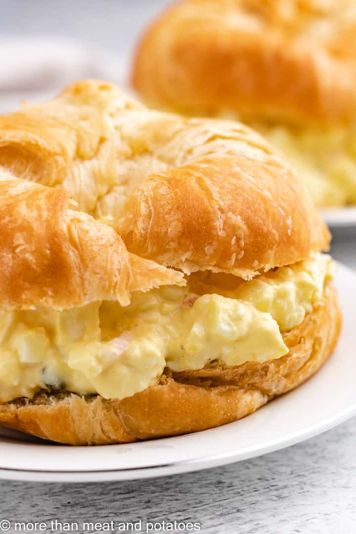 Close up view of egg salad sandwich on a white plate.