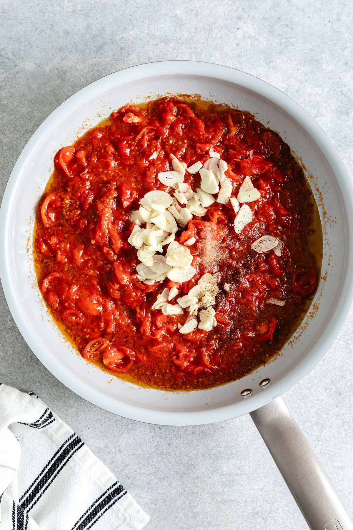 Crushed tomatoes with sliced garlic in a pan.