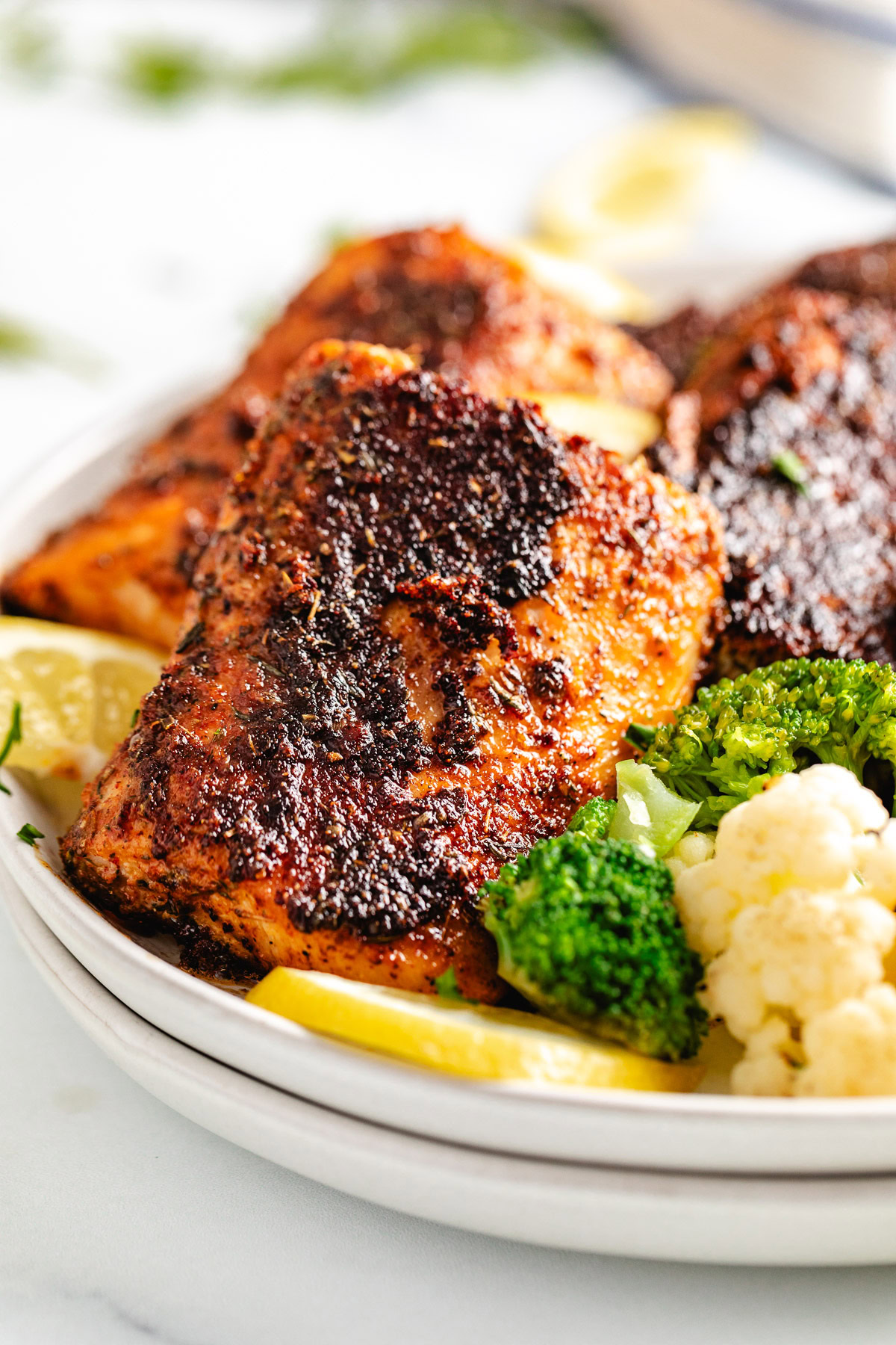 Close up view of blackened mahi mahi next to lemon and veggies.