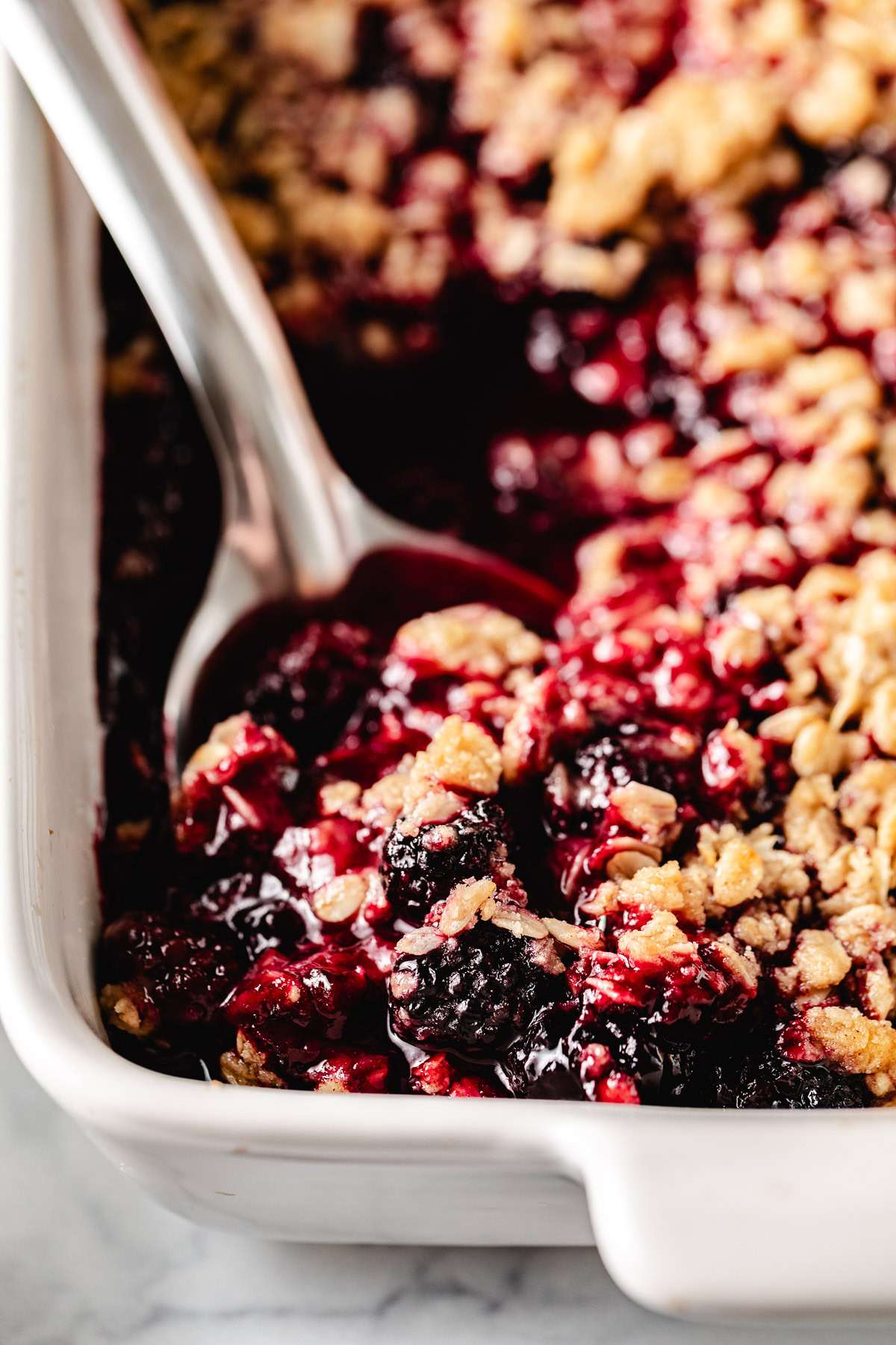 Spoon scooping blackberry crisp from a pan.