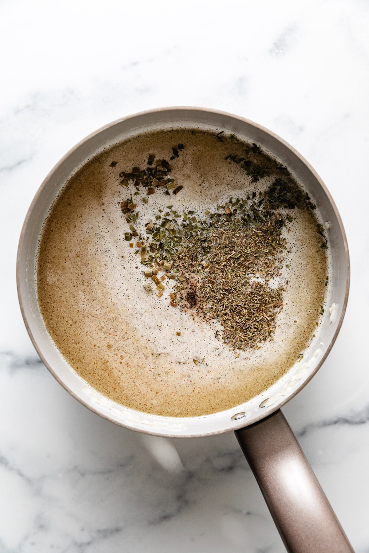 Broth, herbs and rice in a pan.