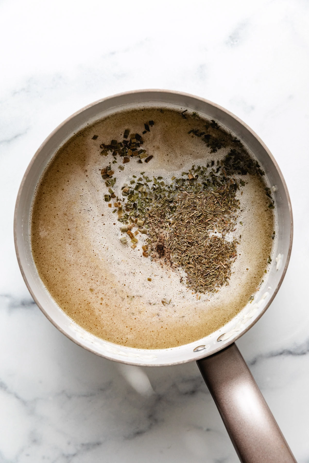 Broth, herbs and rice in a pan.