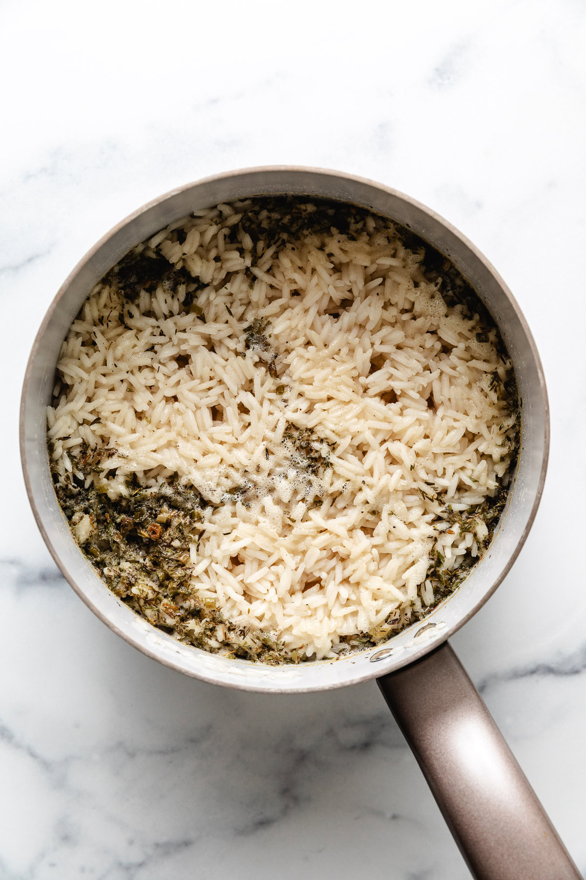 Herbs and rice cooking in a pan.