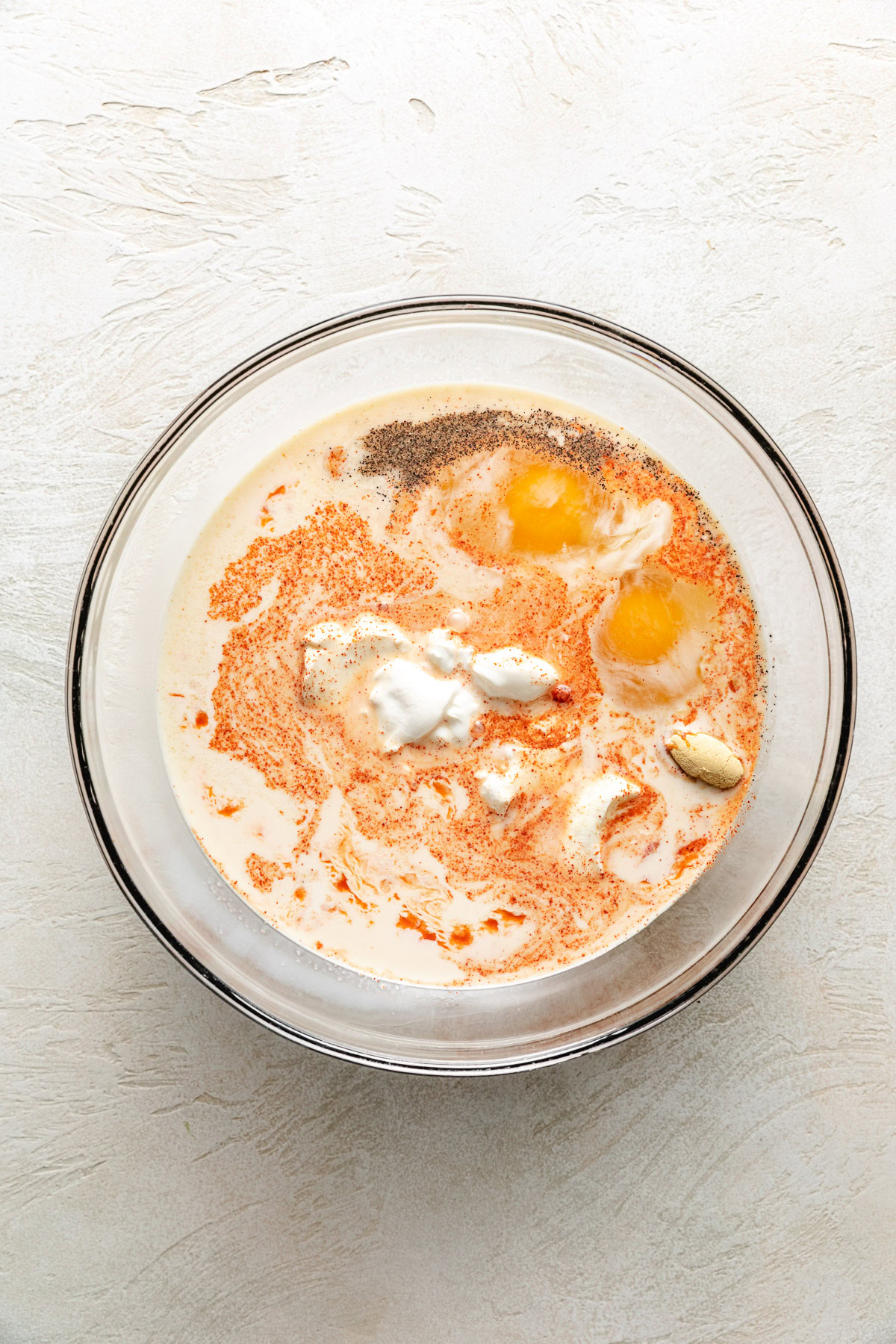 Eggs, milk, spices, and sour cream in a bowl.