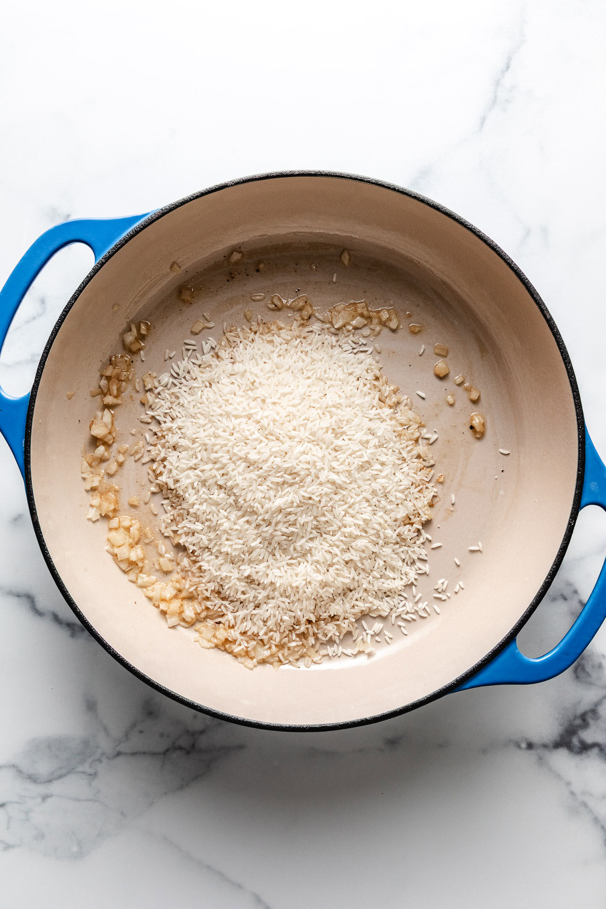 Rice and onions in a skillet.