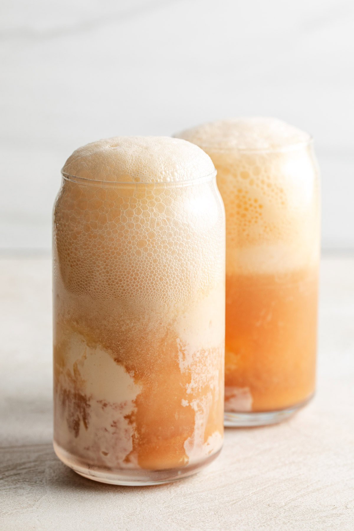 Two glasses of cranberry and orange juice with ice cream.