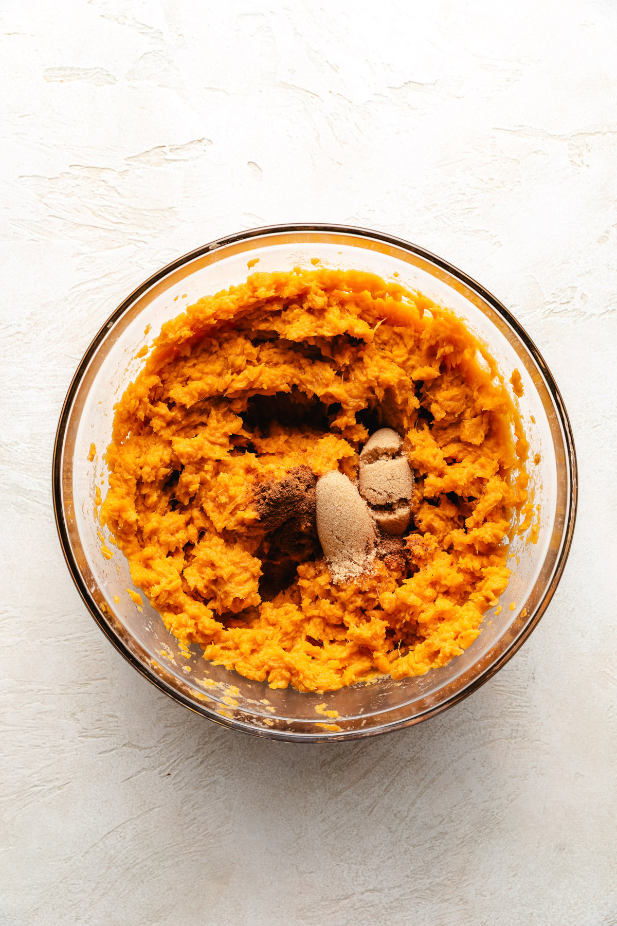 Mixing bowl with sweet potatoes, sugar, cinnamon, and nutmeg.