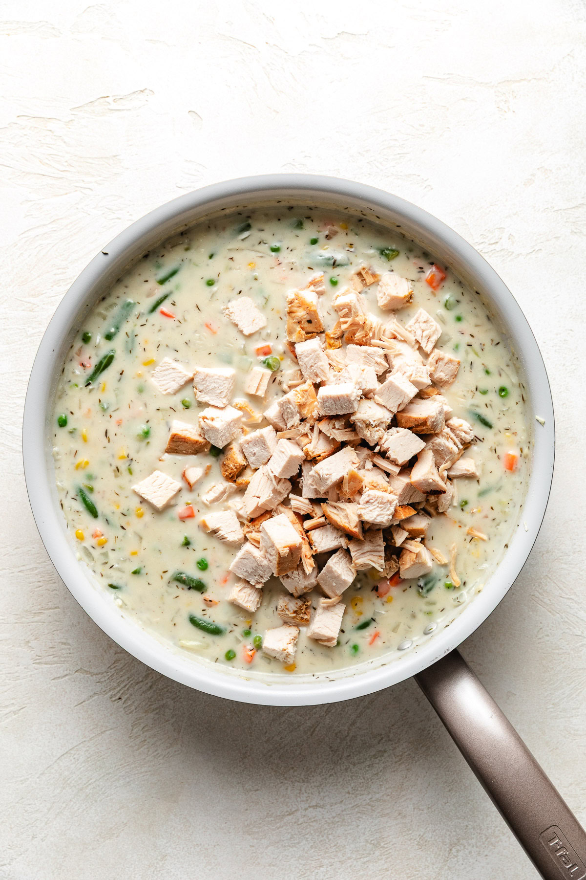 Diced turkey in a skillet of pot pie filing.