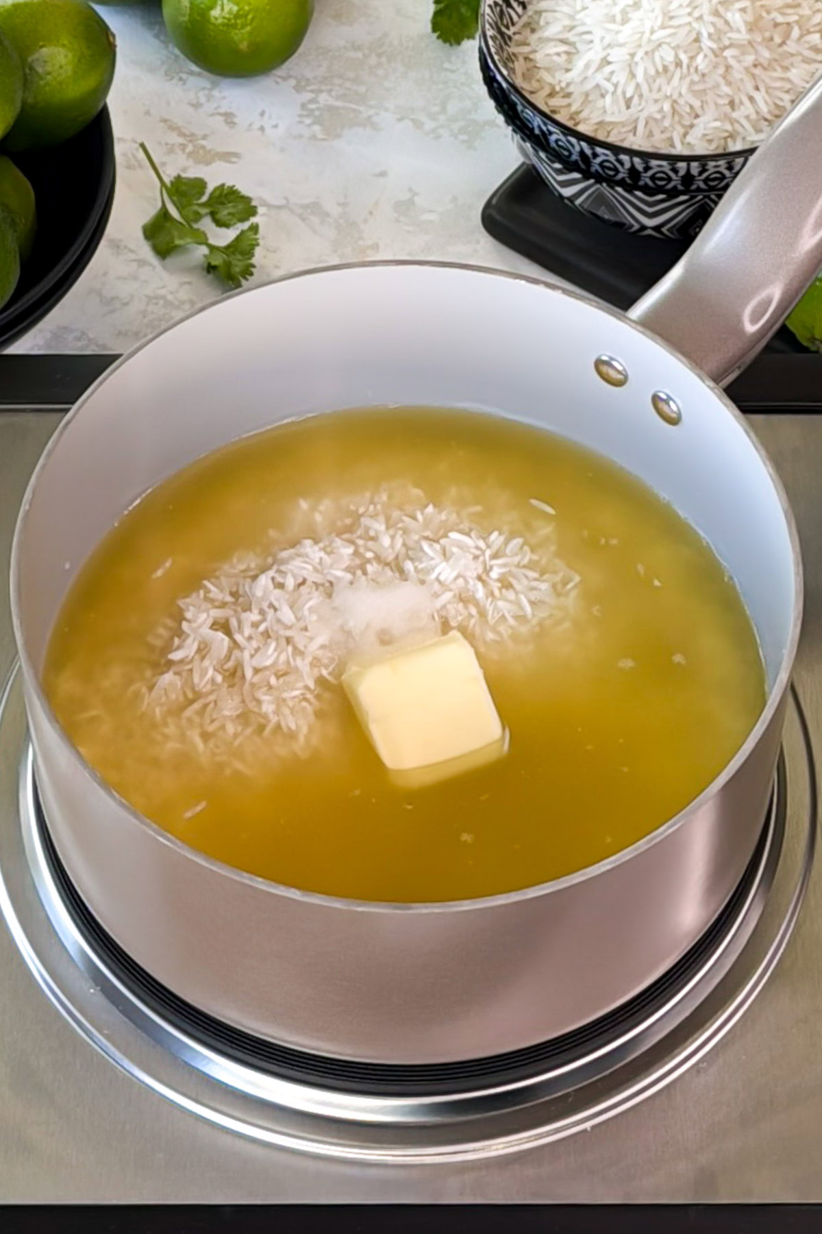Saucepan with uncooked white rice simmering in broth with a pat of butter and salt.