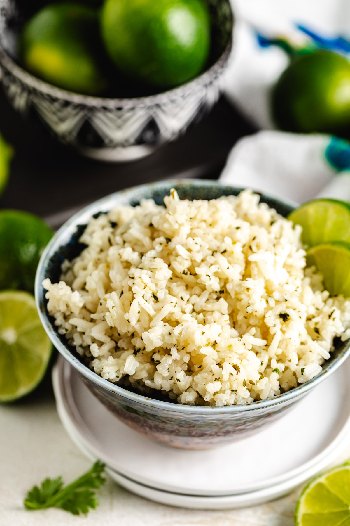 Bowl of fluffy long-grain rice with lime wedges on the rim, with whole limes in the background.