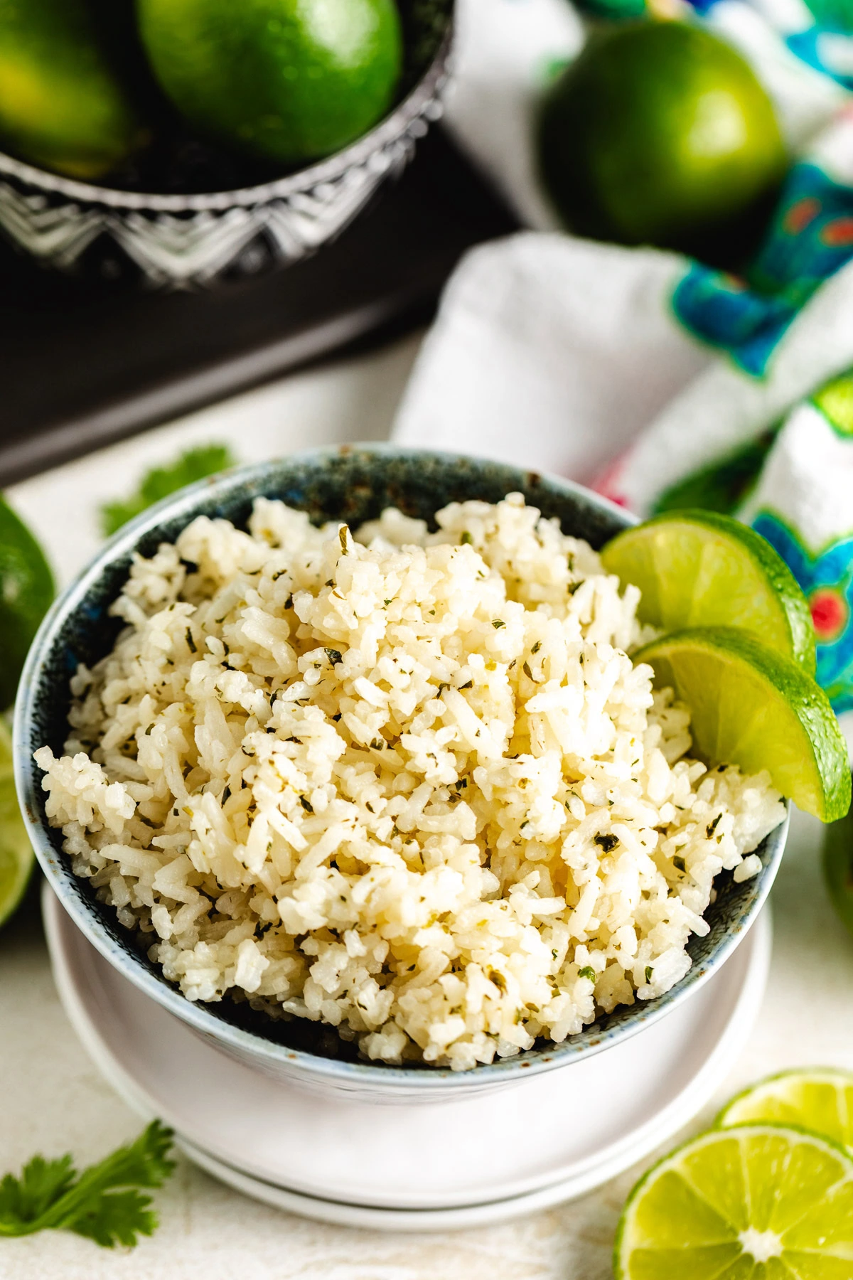 Cilantro lime rice piled in a blue bowl on a white plate with sliced limes and a patterned towel nearby.