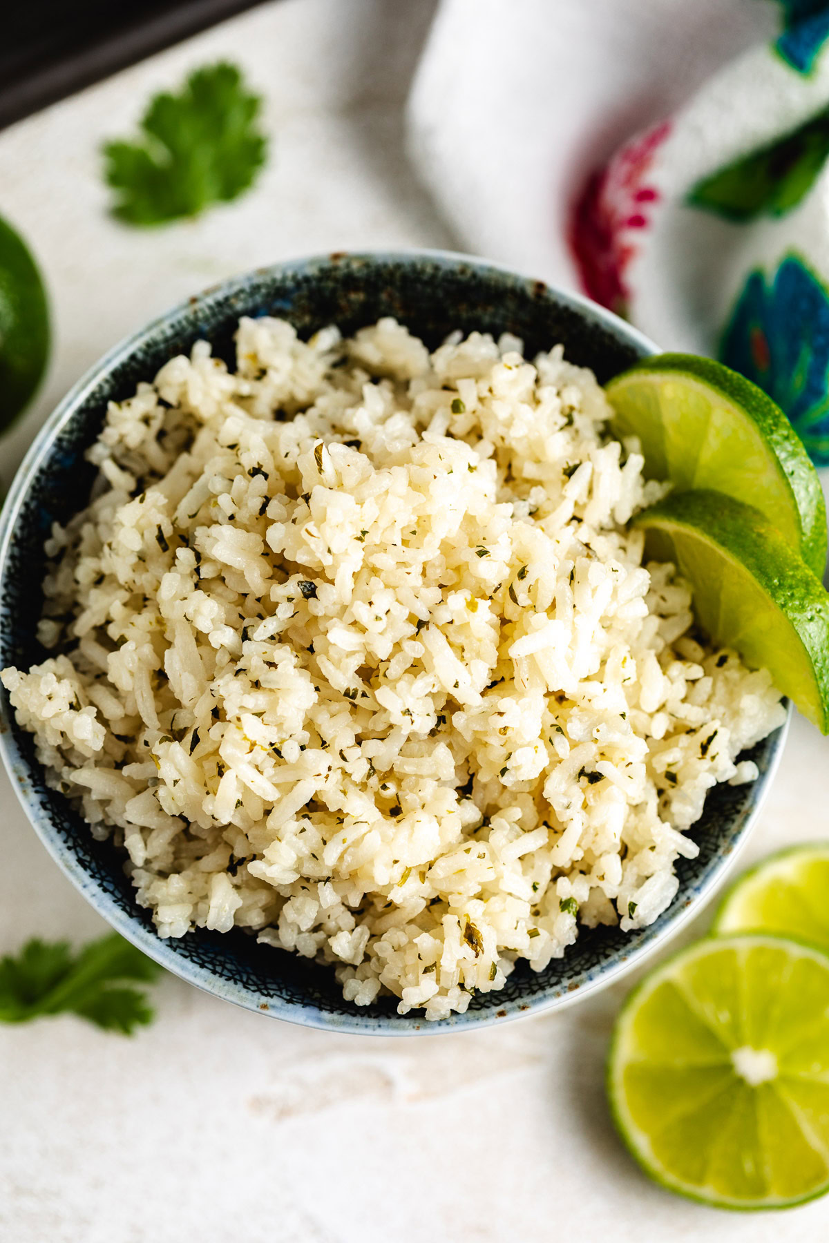 Overhead view of herb-speckled rice in a bowl with lime slices on the side and fresh cilantro on the counter.