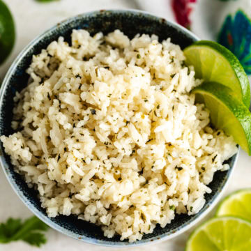 Bowl of cilantro lime rice garnished with lime wedges on a light countertop.