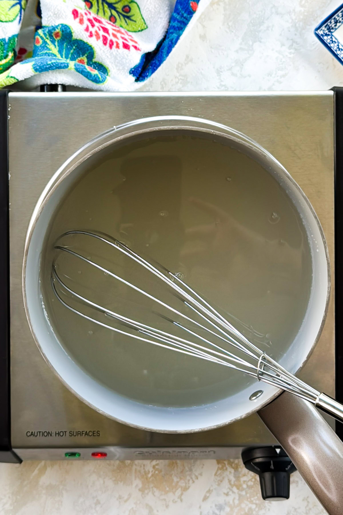A whisk resting in a saucepan of warm sugar syrup.
