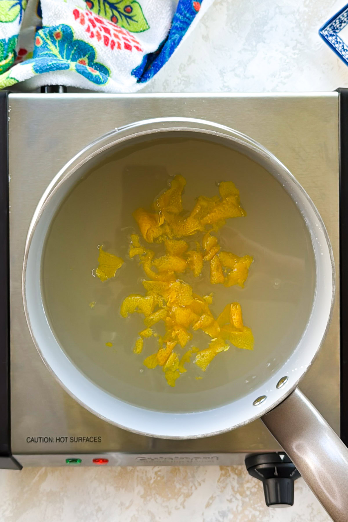 Lemon peel steeping in warm sugar syrup in a saucepan.