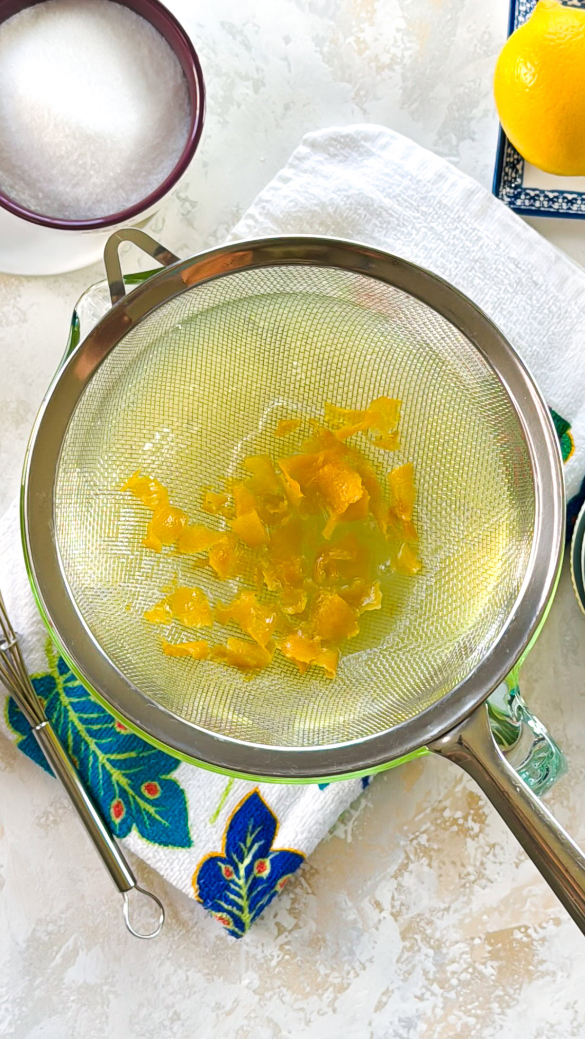 Lemon peel resting in a mesh sieve over a glass measuring cup.