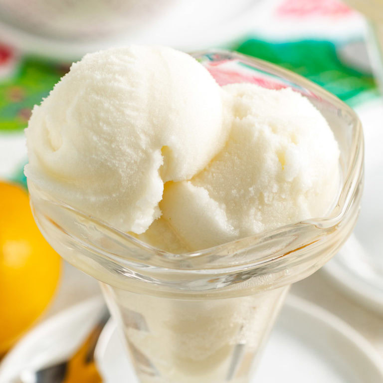 Lemon sorbet scoops in a glass dessert dish on a white plate.