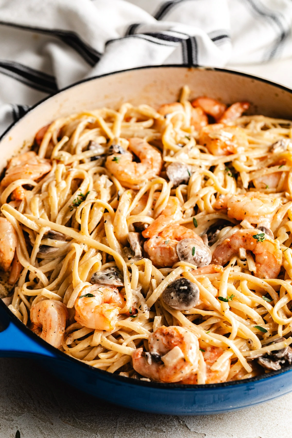 Creamy shrimp and mushroom pasta in a skillet with a black-and-white kitchen towel in the background.