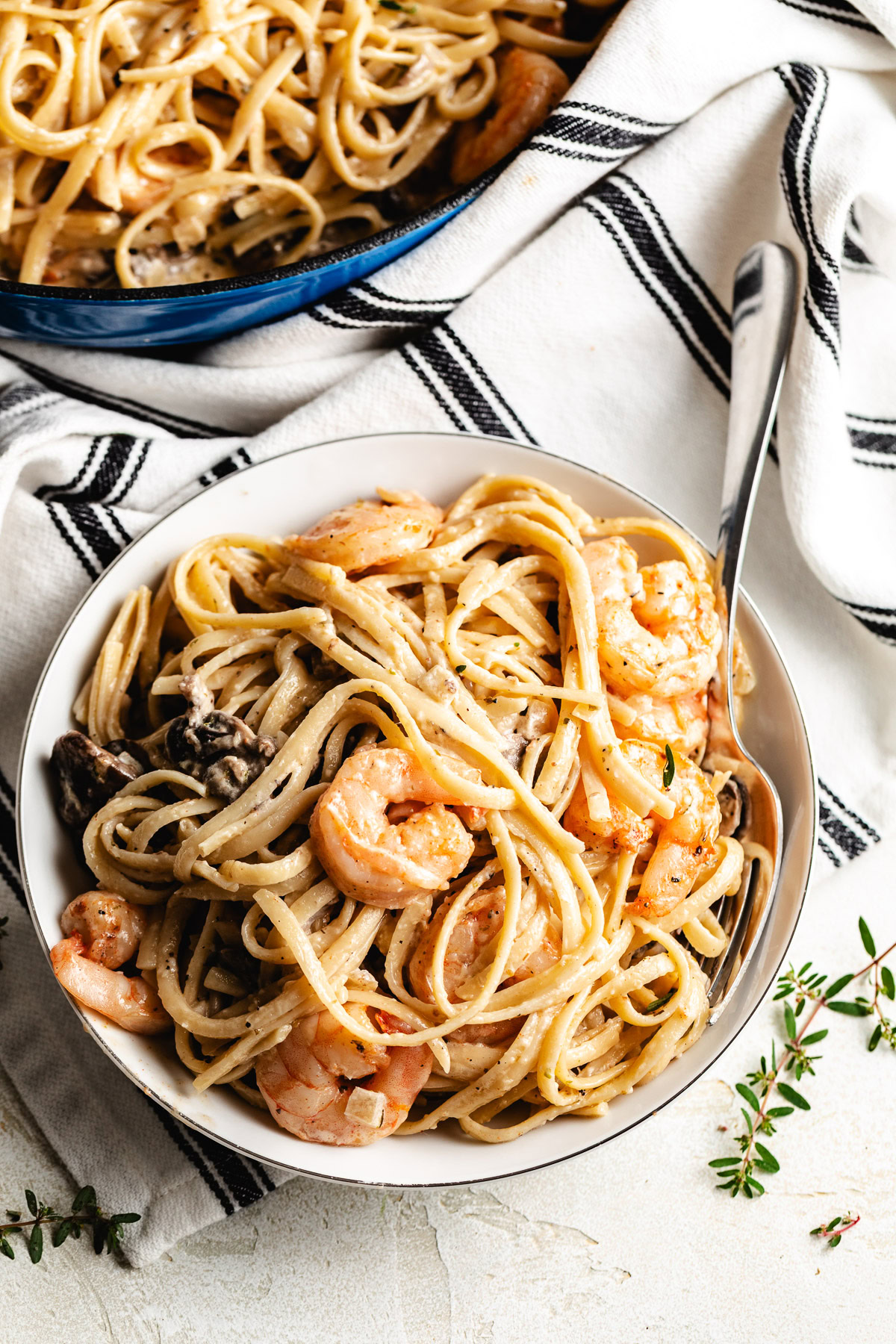 Bowl of mushroom shrimp pasta with creamy noodles and shrimp, skillet in the background.