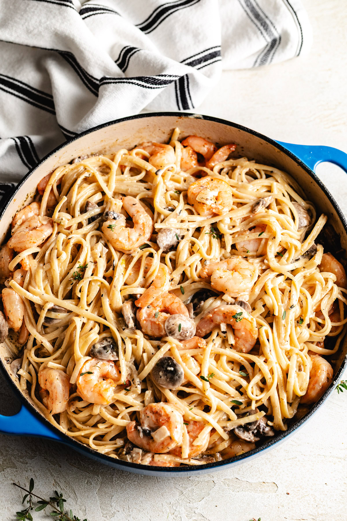 Overhead view of mushroom shrimp pasta in a skillet with herbs and creamy sauce.