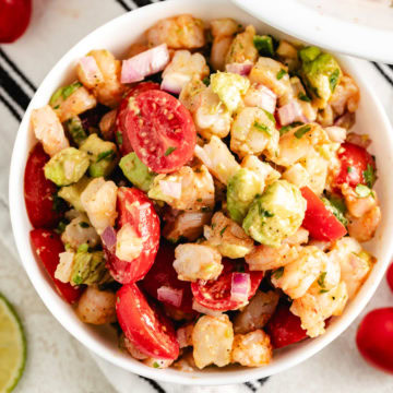 Shrimp and avocado salad with cherry tomatoes, red onion, and a lime dressing in a white bowl.
