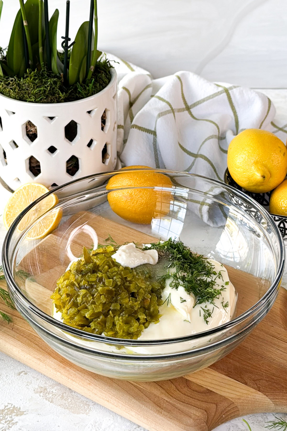 Mixing bowl with mayonnaise, chopped dill relish, lemon juice, and fresh dill ready to be stirred together.