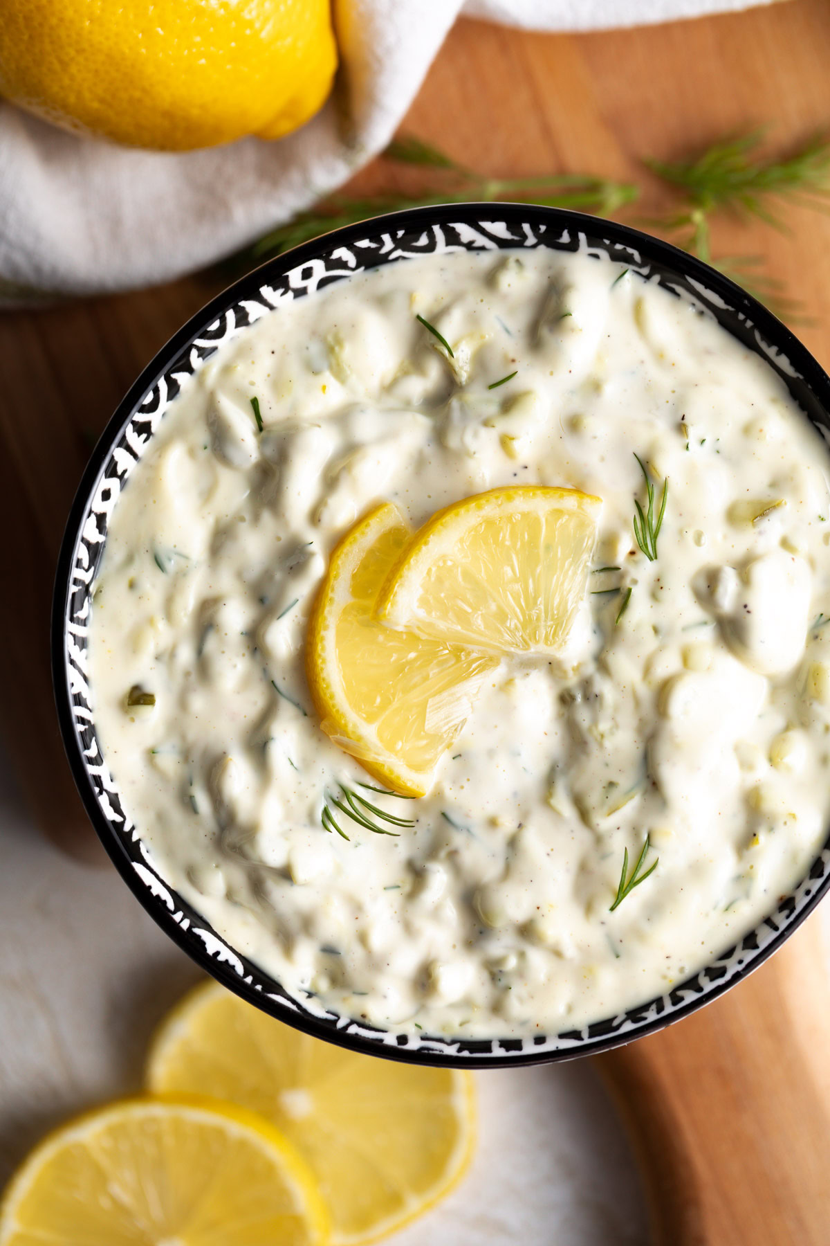 Close-up of creamy dill relish sauce in a patterned bowl, topped with a lemon slice and a few dill sprigs.