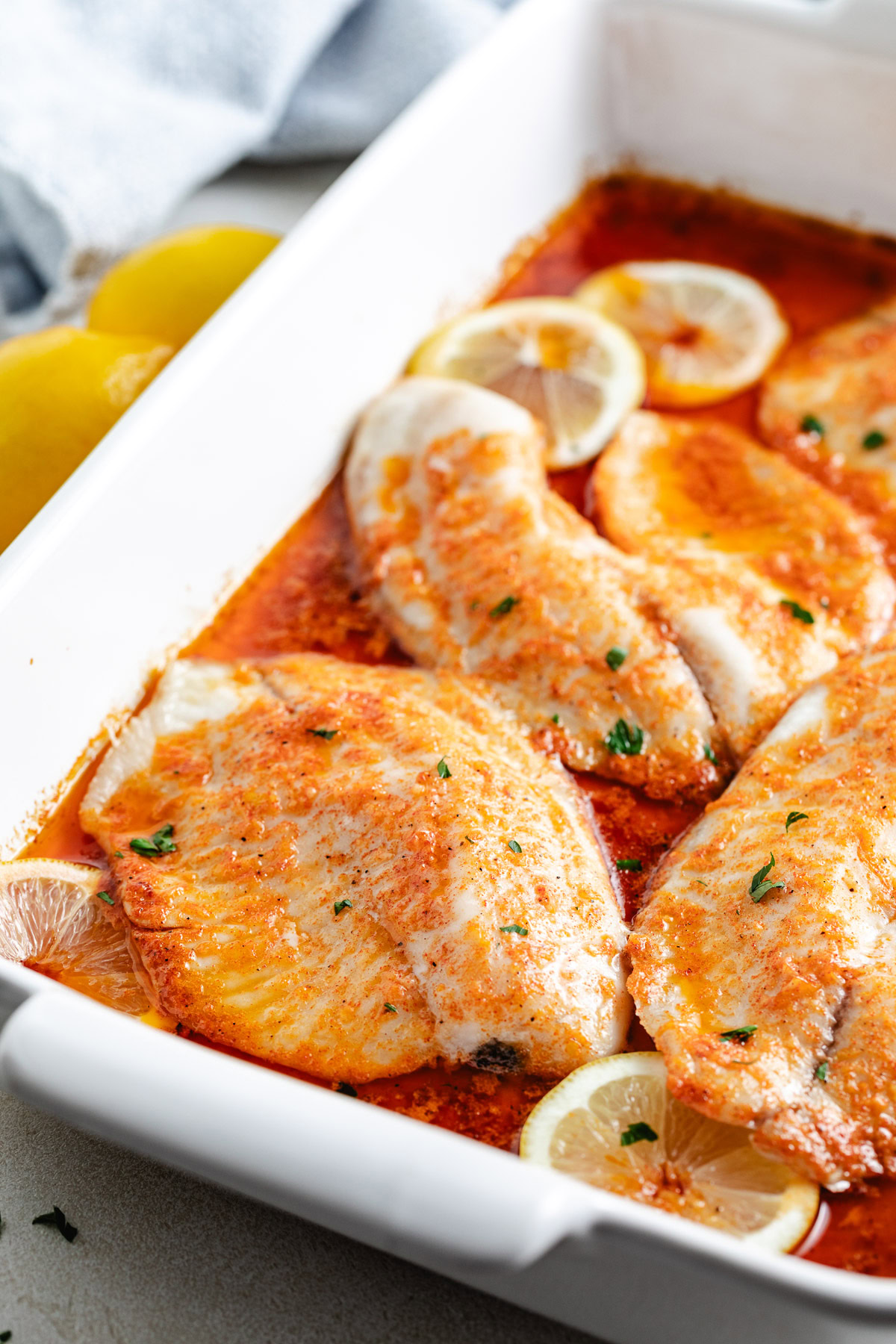 Flaky baked fish and lemon slices in a baking dish.