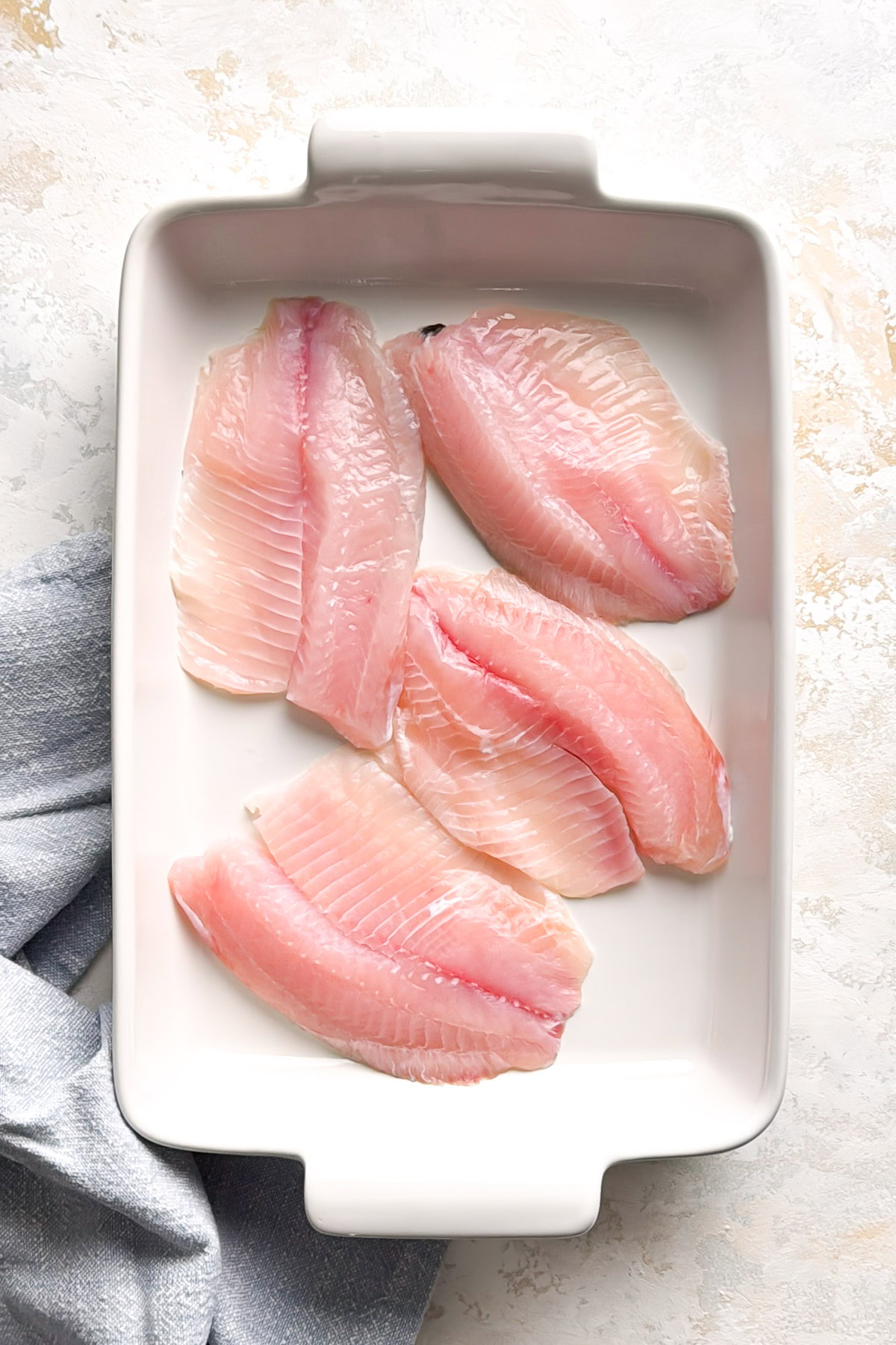 Raw tilapia fillets in a baking dish.